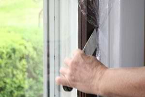 photo demonstrating how to tuck plastic wrap into a gap in a wooden window
