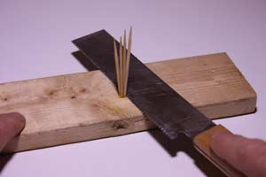 photo using a japan saw to cut toothpicks flush with a wooden board
