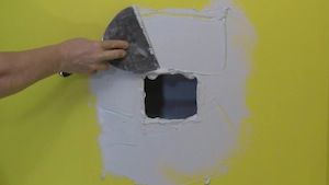 photo spreading joint compound around a wall hole