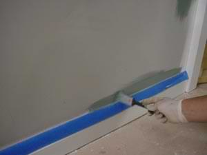 photo using a brush to paint over masking tape on a baseboard