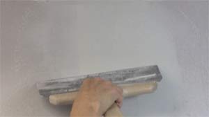 photo skimming joint compound over the center of a drywall butt joint