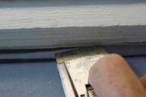 photo demonstrating how to use a razor blade to remove old paint from window glass